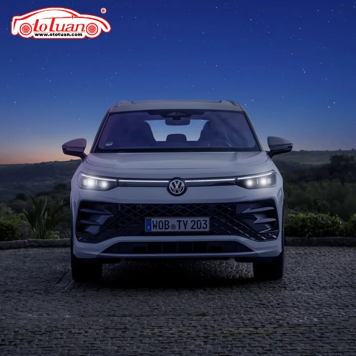 Volkswagen Tayron màu trắng nhìn chính diện với cụm đèn trước bật sáng trong khung cảnh chạng vạng.