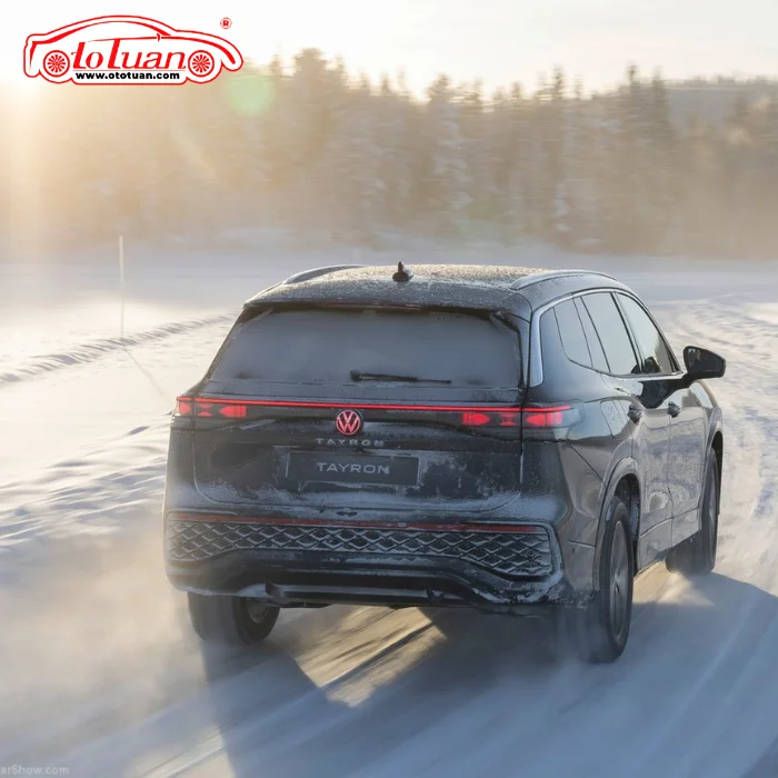 Volkswagen Tayron màu tối nhìn từ phía sau đang di chuyển trên đường phủ tuyết dưới ánh nắng.