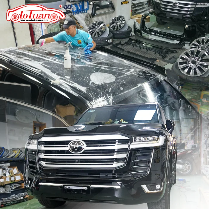 Kỹ thuật viên thao tác với lớp phim trong suốt trên nóc xe, ghép cùng ảnh Toyota Land Cruiser màu đen